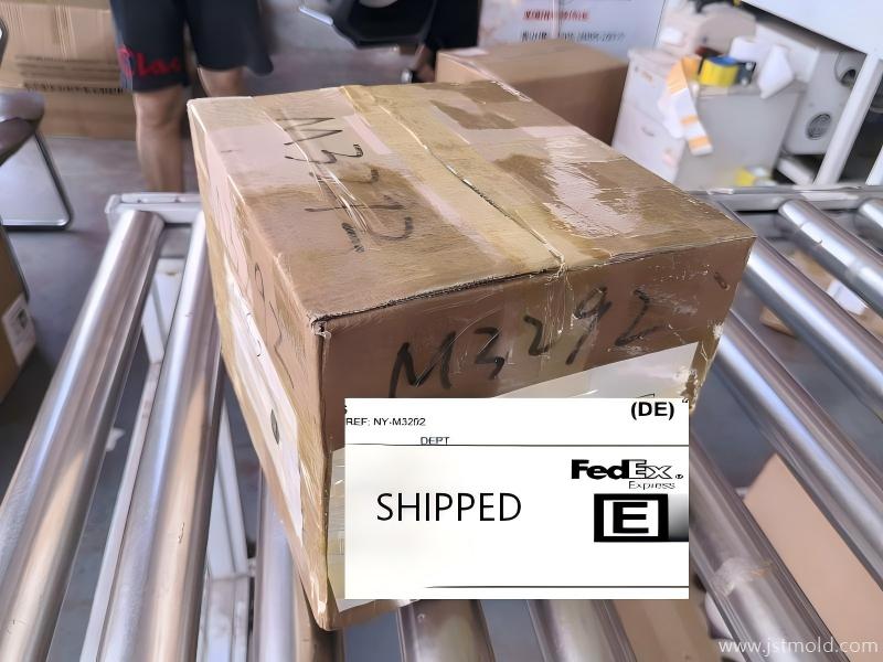 A shipping box with 'DE' and 'SHIPPED' labels on a factory line.